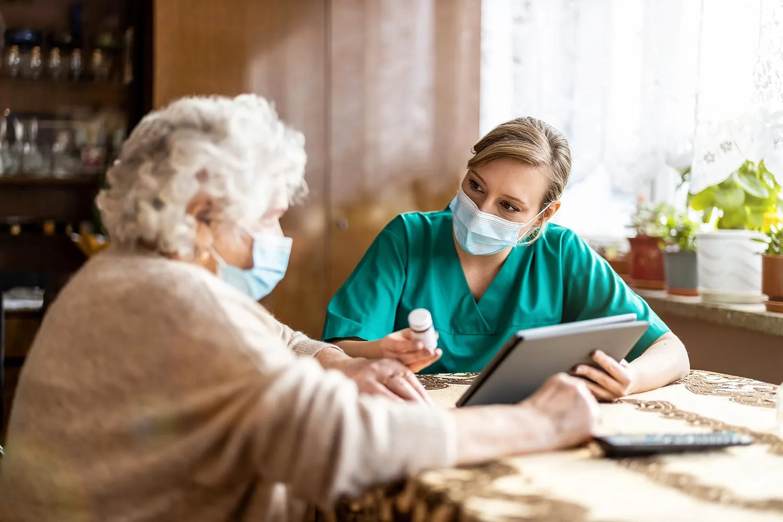 Female nurse reviewing prescription bottle with senior patient